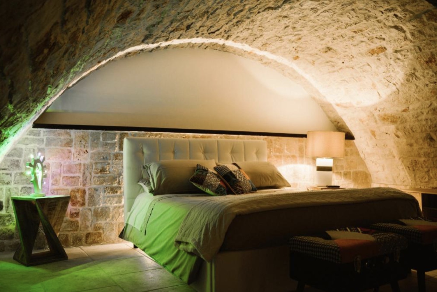 La camera da letto sotto l'arco in pietra, con testiera capitonné e luce d'atmosfera