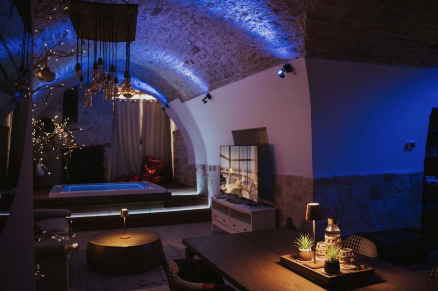 L'ambiente living sotto la volta illuminata di blu, con lampade sospese e vasca sullo sfondo