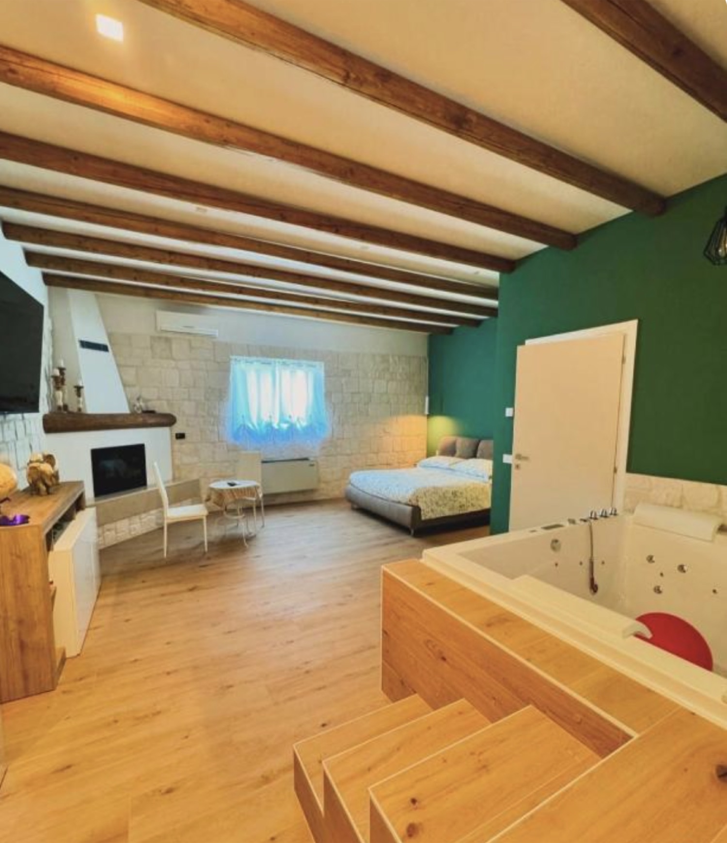 Vista d'insieme della suite, con travi in legno, letto e vasca idromassaggio