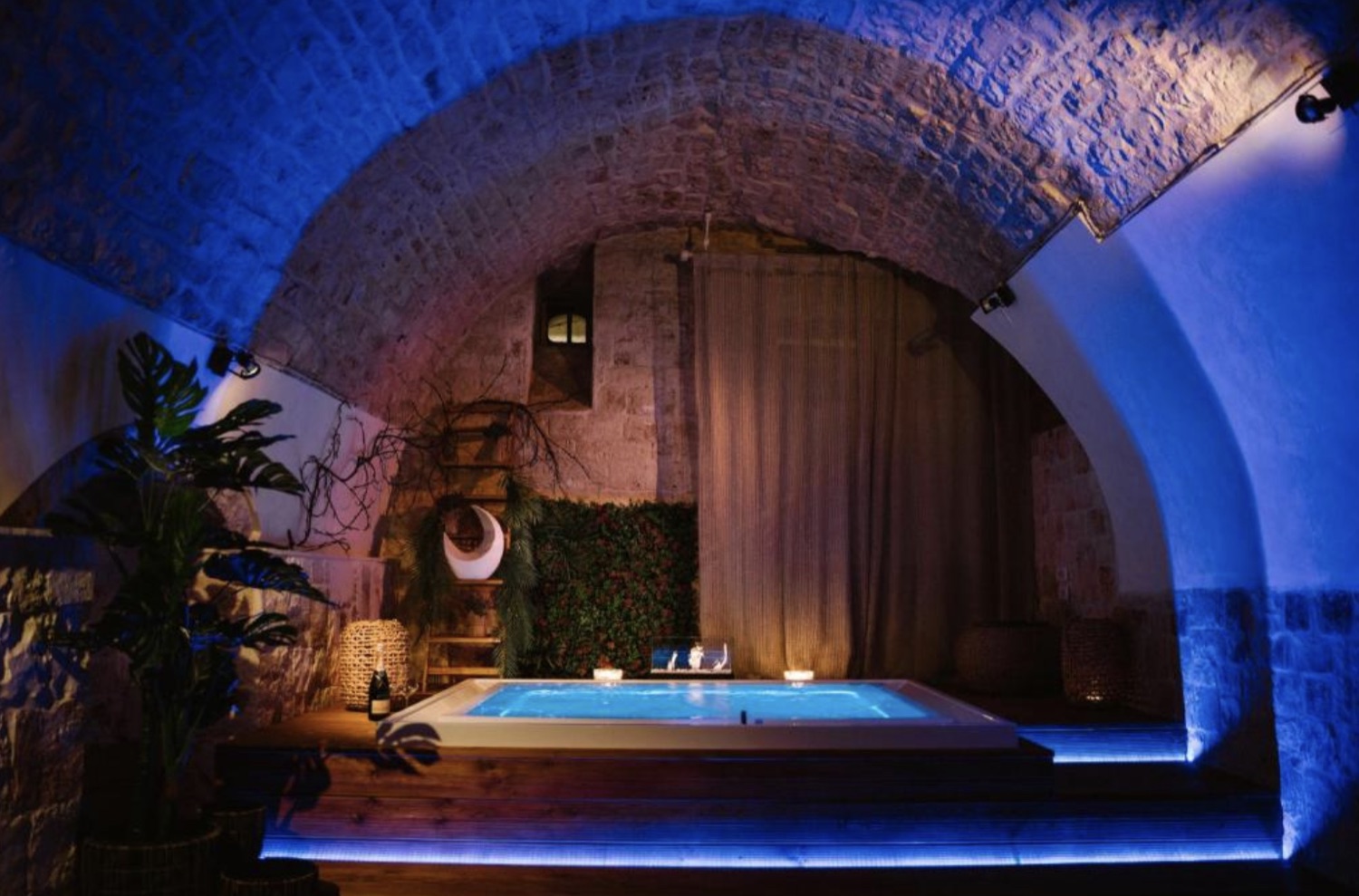 La vasca idromassaggio sotto la volta a botte in pietra, avvolta da luci blu